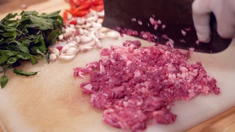 hand with glove chopping raw beef with pad kra paw ingredient on white chopping board, close up