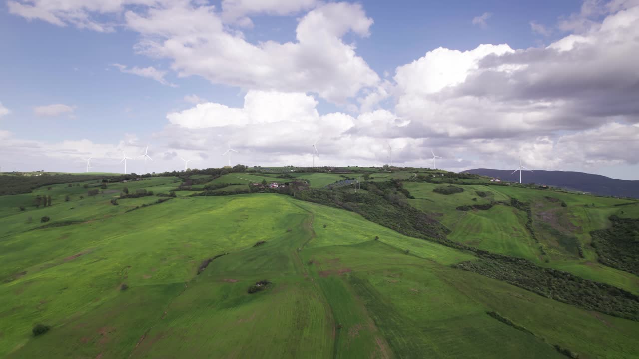 Aerial view of wind turbine generating sustainable energy on a green hill at horizon, wide angle