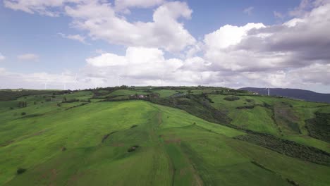 aerial view of wind turbine generating sustainable energy on a green hill at horizon, wide angle