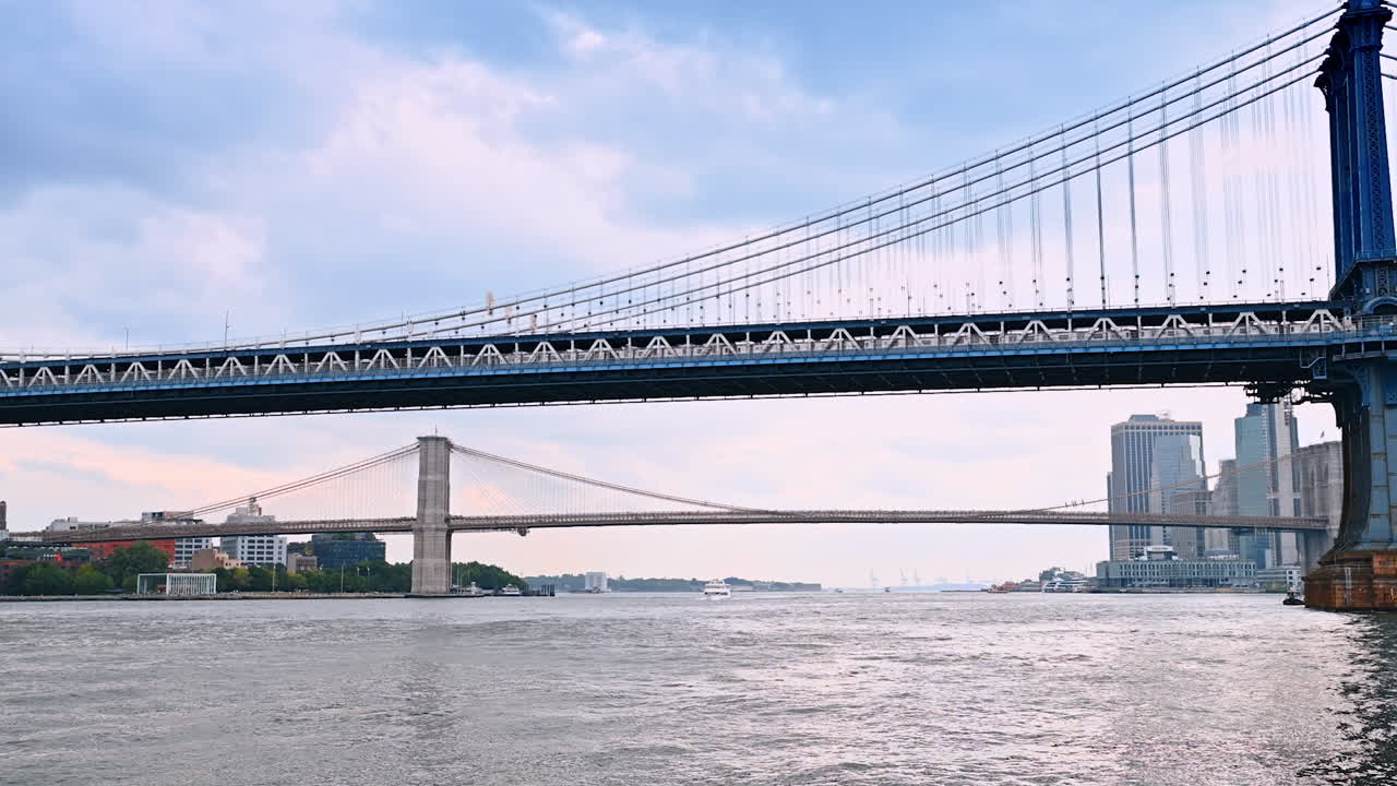 Train runs by the Manhattan Bridge. Low angle view from the waterscape. The Brooklyn Bridge at backdrop. New York, USA