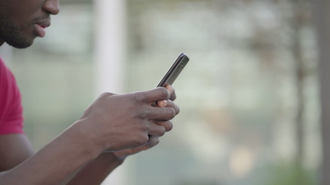Primo piano delle mani di un giovane uomo che digita sullo smartphone al parco.