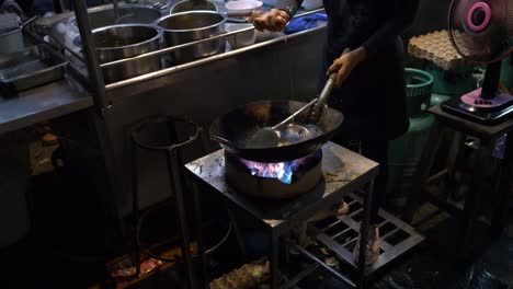 Chef-cracking-an-egg-in-a-wok-with-blazing-fire,-street-food-in-Chiang-Mai,-Thailand,-slow-motion-video