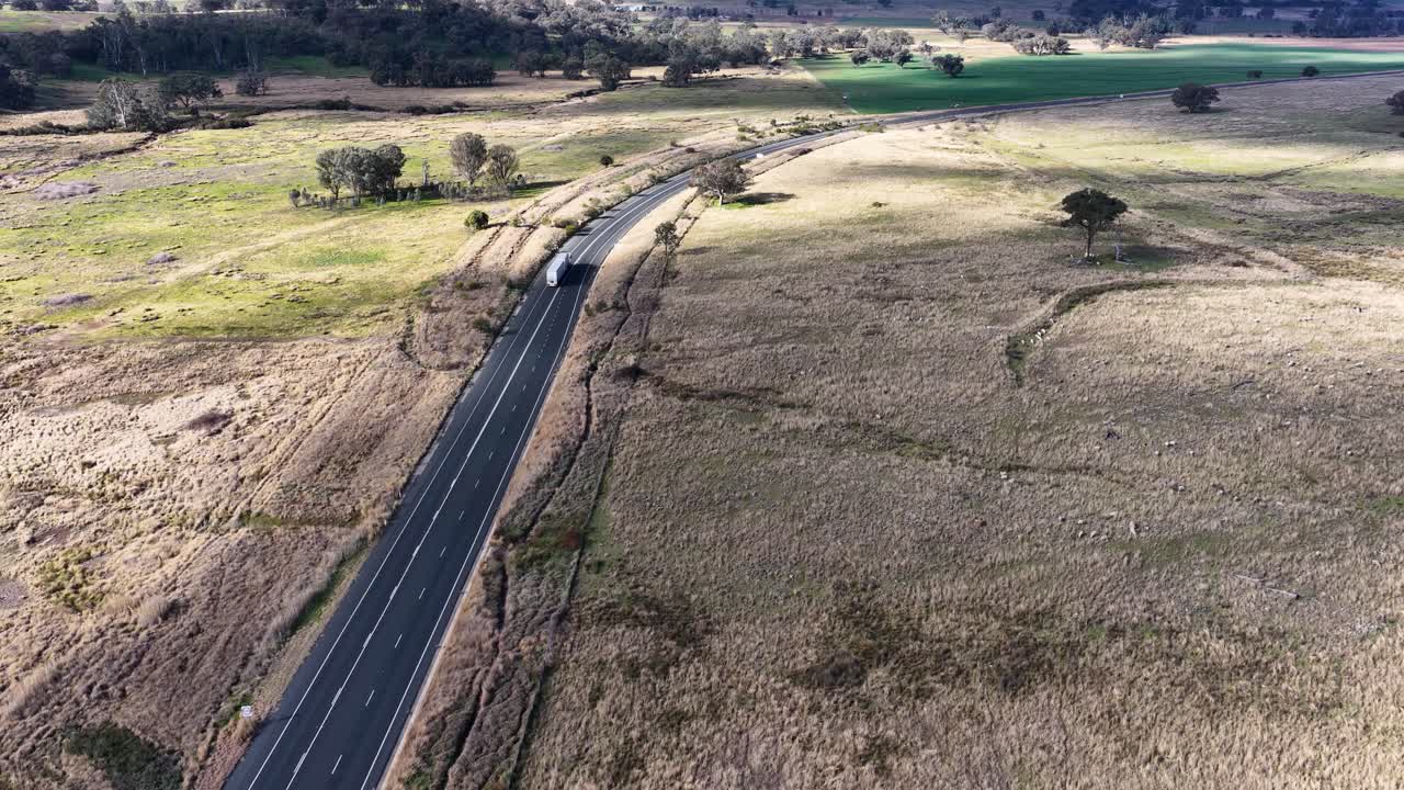 Drone footage tracks vehicles traveling along a winding asphalt road through open countryside near Coonabarabran, New South Wales, under natural daylight with smooth camera movement