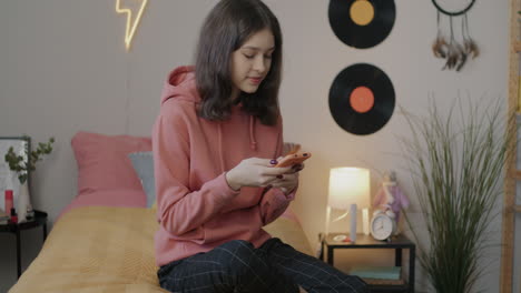 una adolescente usando un teléfono inteligente en el dormitorio
