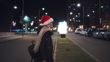 a beautiful woman in a santa claus hat walks at night on christmas