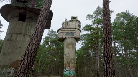 Establishing-aerial-view-of-old-Soviet-military-concrete-observation-watchtower,-pine-tree-forest,-Liepaja-,-military-heritage,-Nordic-woodland,-wide-drone-shot-moving-backward-low