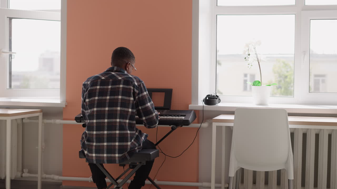 estudiante entretiene con sintetizador en casa. instrumentista afroamericano practica una pieza musical usando un dispositivo eléctrico en una habitación de albergue bien iluminada