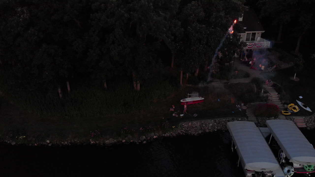 drone volando a un hombre disparando fuegos artificiales de velas romanas desde la costa sobre un lago el 4 de julio