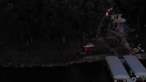 Drone-flying-a-man-shooting-roman-candle-fireworks-from-shore-over-a-lake-on-the-4th-of-July