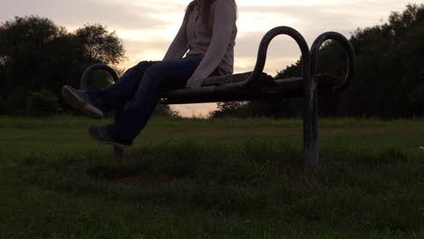 piernas y pies de mujer sentada en un banco del parque al atardecer