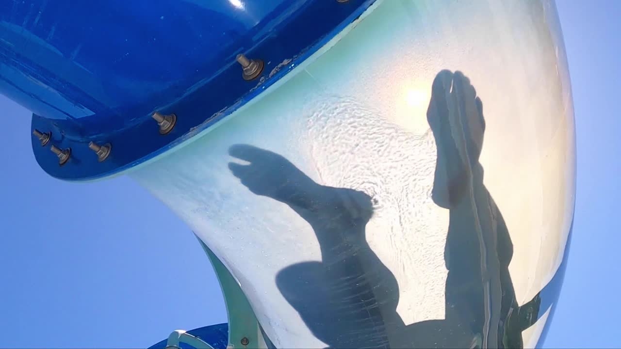투명한 워터 슬라이드 아래, 슬로우 모션으로 터널을 미끄러지는 두 사람의 실루엣