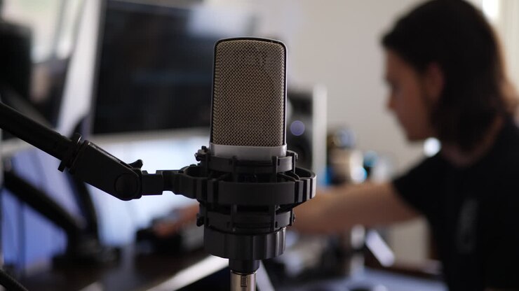 Un produttore musicale uomo alla sua scrivania dello studio di registrazione musicale con un microfono a condensatore per registrare un cantante o una voce. SCORRI A SINISTRA
