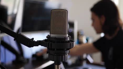 a male music producer at his music recording studio desk with a condenser microphone for recording a singer or vocalist slide left