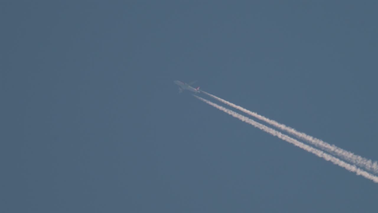 Airplane flying high above leaving long contrails in a clear blue sky