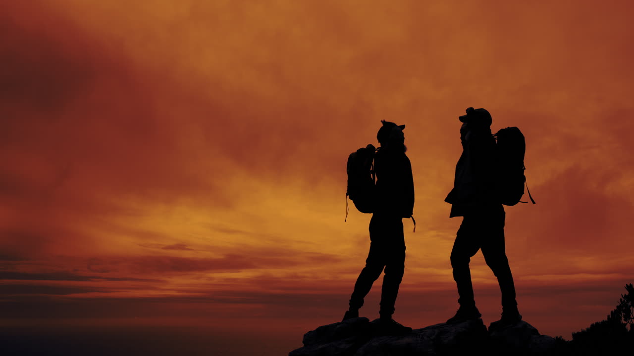 Silhouette of two hikers on a mountain top at sunset