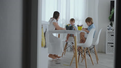 familia feliz joven madre hermosa y dos hijos dibujan con lápices de colores sentados en la mesa en la cocina. la cámara se mueve en cámara lenta