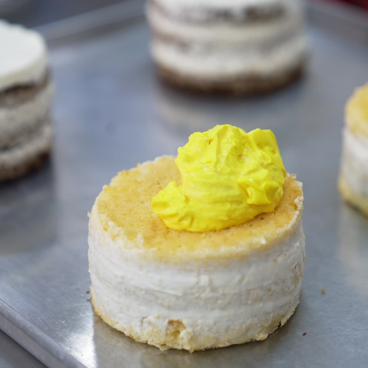 Little vanilla sponge cake is covered with bright yellow butter cream. Desserts decoration at modern food factory. Close up