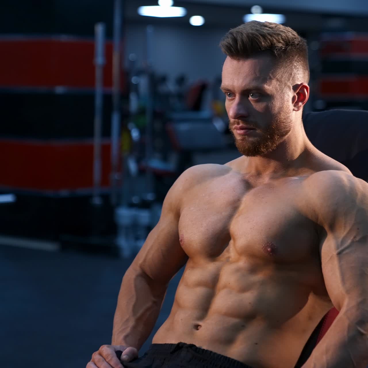 Allenatore di fitness forte e attraente si siede su una panca sportiva e si riposa dopo aver allenato i muscoli. Busto con muscoli perfetti.