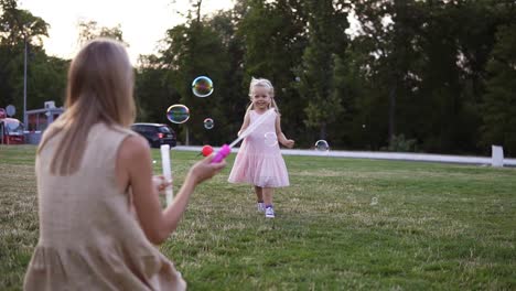 Mother-And-Her-Little-Daughter-Playing-Together,-Blowing-And-Baby-Catching-Soap-Bubbles