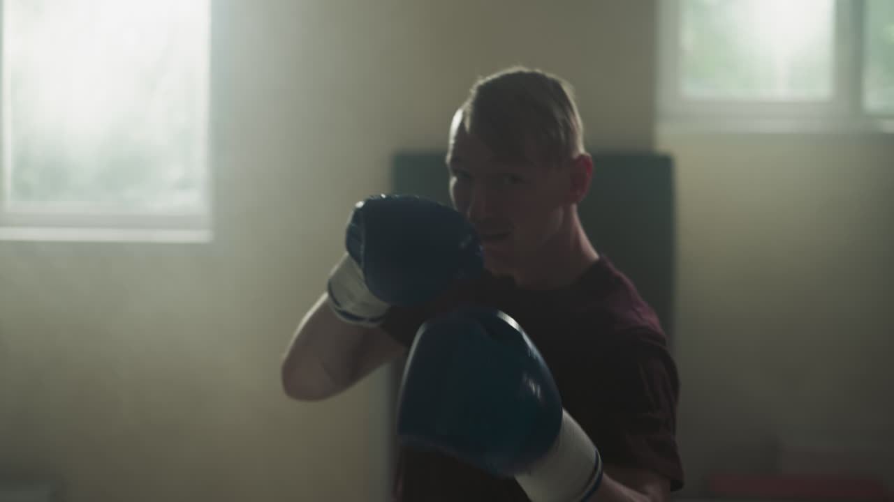 스포츠 클럽에서 후크와 업퍼커트 훈련을 하는 스포츠 선수. 진지한 권투 선수는 체육관에서 스로우 모션으로 카메라에 주먹을 니다. 운동 기간을 싸우고 있습니다.