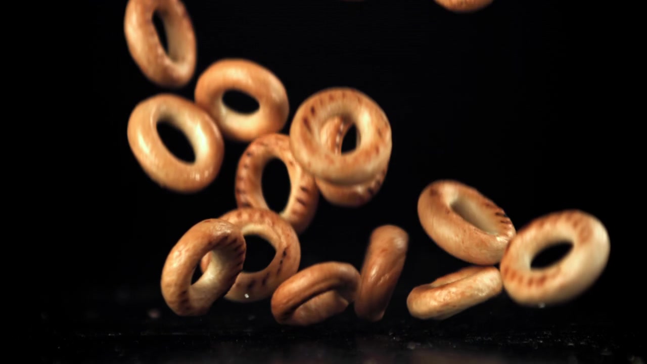 Slowmotion af små bagels, der falder ned på en sort baggrund.