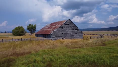 drone footage over a rustic vintage abandoned barn in a field in the summertime