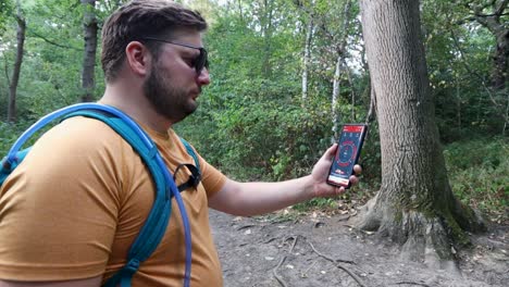 Young-man-with-a-backpack-and-sunglasses-lost-alone-looks-at-the-compass-and-walks-into-the-woods