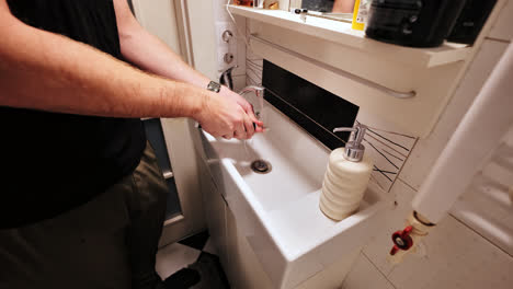 close up of man rinsing electric toothbrush in sink with soap dispenser nearby