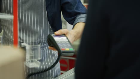 un cliente sonriente está dando una tarjeta de crédito al cajero para pagar productos alimenticios en el supermercado.