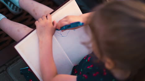 little girl draws funny sun in copybook sitting on pavement