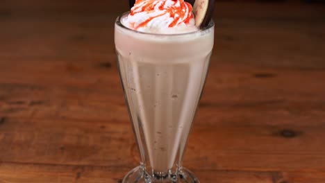 detailed close up of a chocolate milkshake, with caramel, espresso and whipped cream, tilted up and down on a table