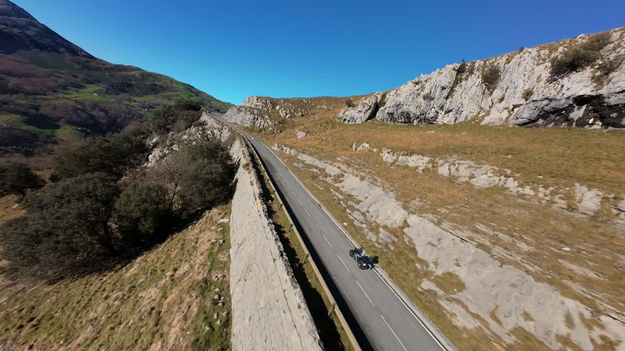 FPV drone chase of a motorbike navigating a mountain road curve in Cantabria. Mist drapes the surrounding valley, enhancing the cinematic atmosphere.