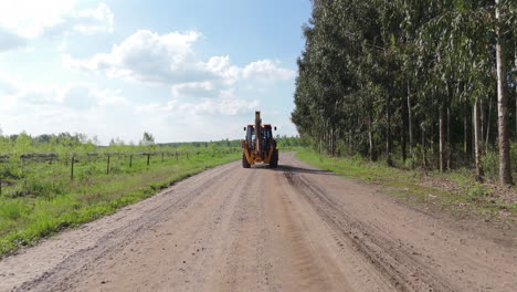 aerial rearview tracking, tractor driving on a dirt road by green field, traveling to work site, surrounded by open farmland