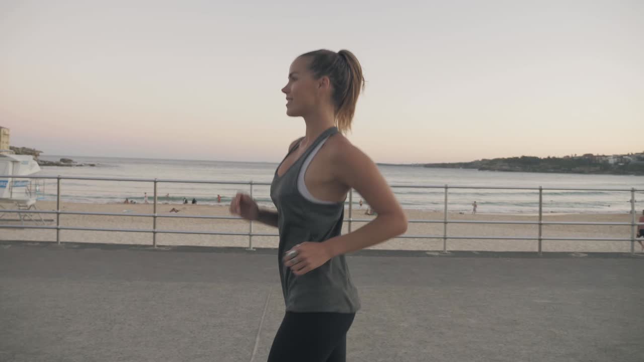 una hermosa mujer corriendo por la tranquila playa durante la puesta de sol en bondi, australia - cámara lenta