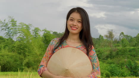 Mujer-Campesina-Vietnamita-Parada-En-Una-Plantación-De-Arroz-Con-Sombrero-De-Bambú-Sonriendo-A-La-Cámara