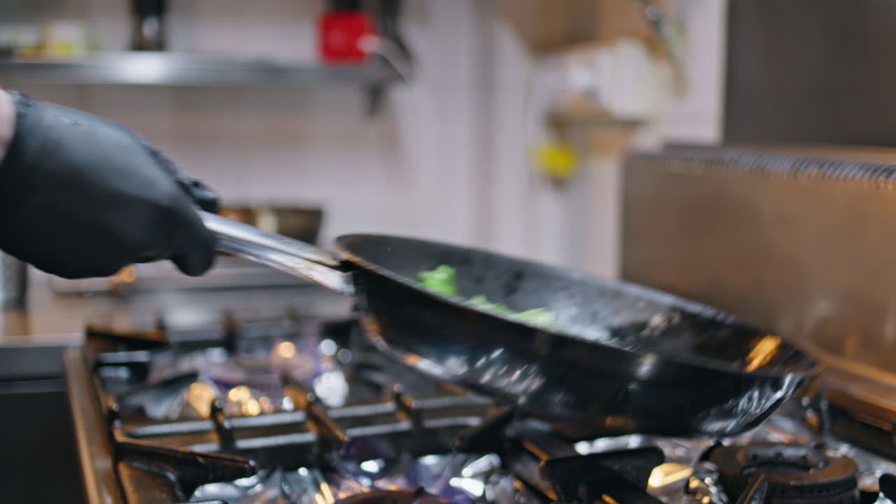 Chef cooking greens pan over flame stove modern kitchen closeup. Unknown man