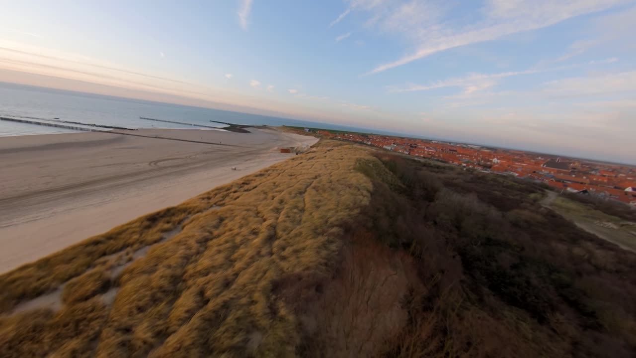 volando sobre las dunas revelando un pequeño pueblo detrás del dique en los países bajos