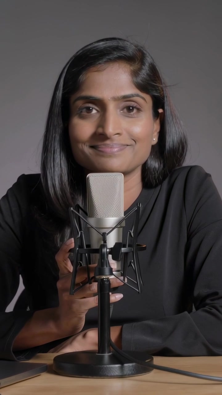 Vertikal video: Kameraet kører, indisk vært i sort top taler ind i en mikrofon i et studie til en podcast.