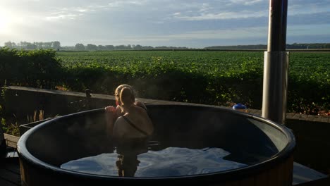 woman relaxing on an outdoor traditional hot tub while admiring the greenery plant