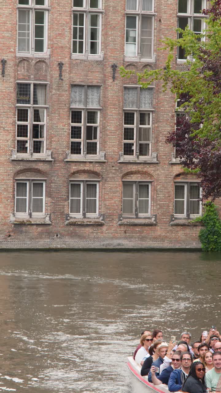 Turisti si godono un giro in barca sul canale oltre l'antica architettura in mattoni, luce diurna nuvolosa, telecamera statica.