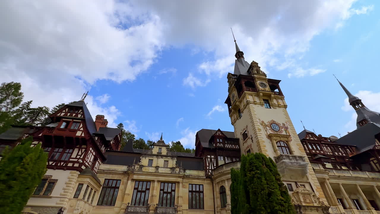 Beautiful façade of the Peles Castle in Sinaia, the Carpathians, Romania. Low angle view. Clouds in the blue sky at backdrop