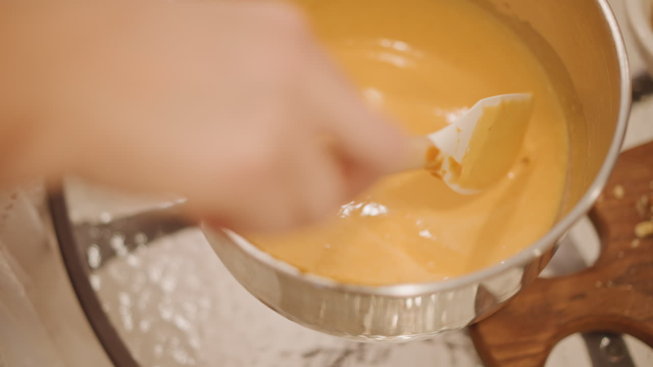 Warm pumpkin custard finished by hand home cook gently smooths thickened pumpkin custard in saucepan over simmering water, spatula glides across glossy surface, wooden board base, closeup of hands