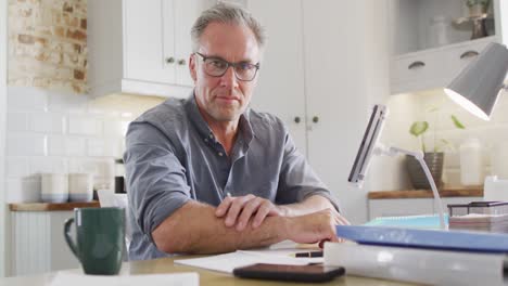 Portrait-of-happy-caucasian-man-sitting-at-table-in-kitchen,-looking-at-camera-and-smiling