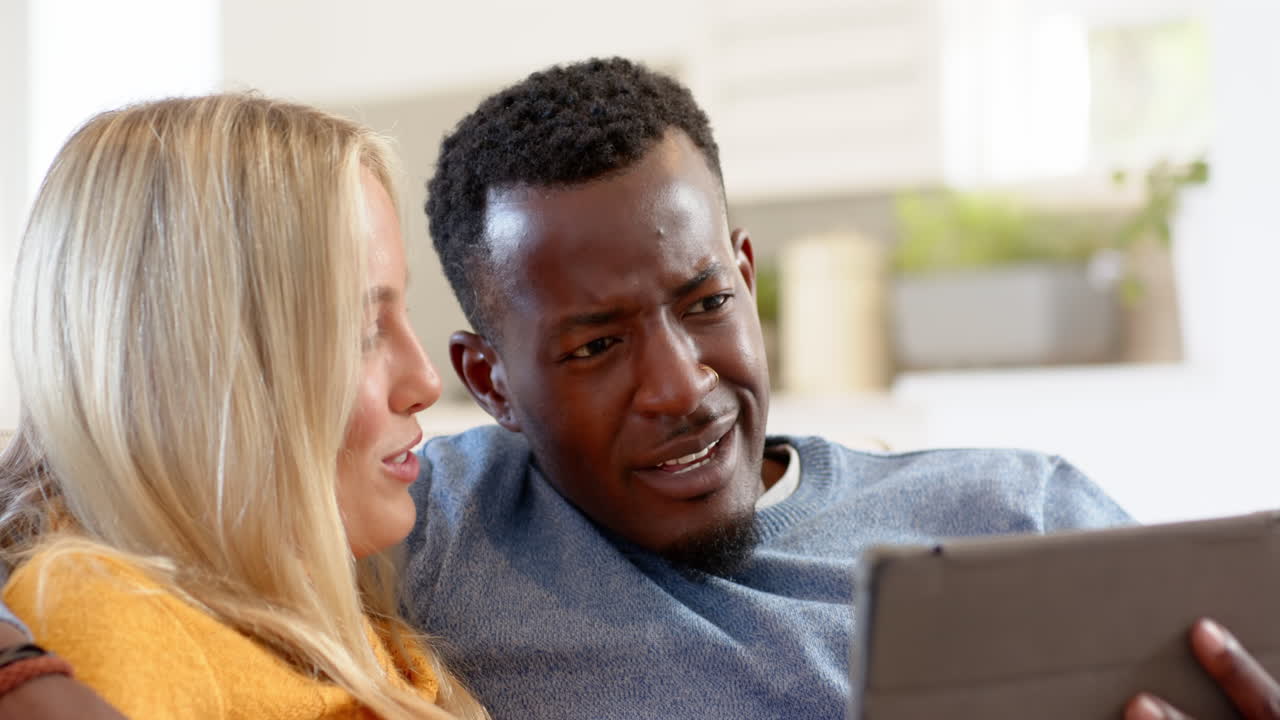 Happy diverse couple enjoying time together at home with tablet