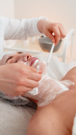 terapia enzimática esteticista aplicando crema médica hidratante en la cara de una mujer joven adulta con pinceles