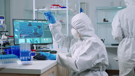 scientist nurse in ppe suit taking notes on computer looking at test tube