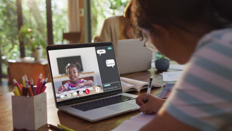 schoolgirl using laptop for online lesson at home, with school friend and web chat on screen