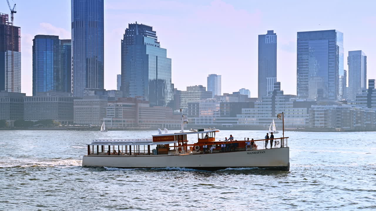 One-deck riverboat moves by the river at daytime. Hazy skyline of modern New York, USA at backdrop