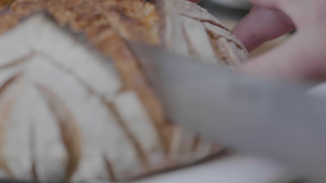 Extreme close-up rack focus of a knife cutting through a loaf of artisan bread