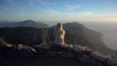 slowmotion pulling in towards a young blonde woman sitting and looking the view on the table mountain during sunset